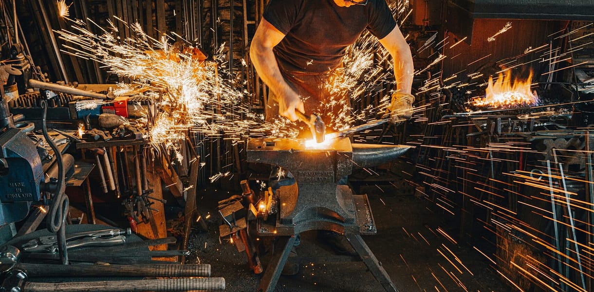 A Blacksmith forging, creating something, the sparks indicative of intentional blows