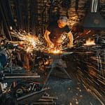 A Blacksmith forging, creating something, the sparks indicative of intentional blows