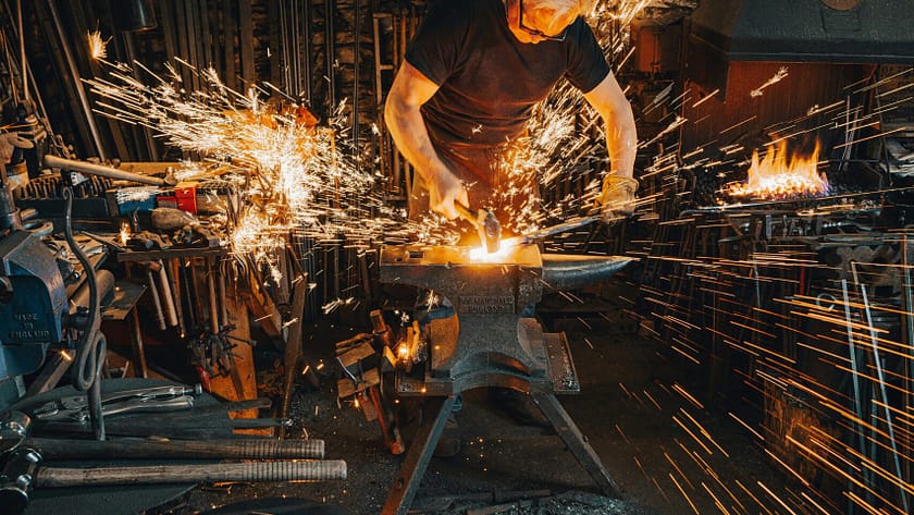 A Blacksmith forging, creating something, the sparks indicative of intentional blows