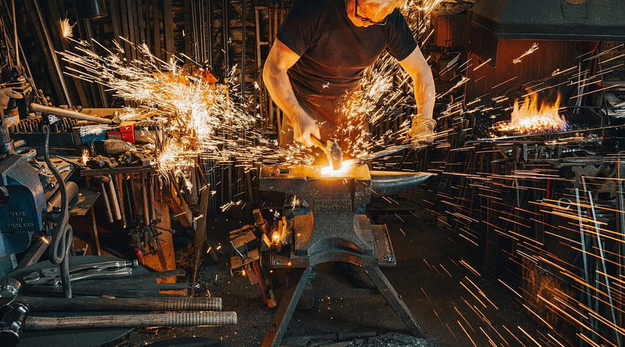 A Blacksmith forging, creating something, the sparks indicative of intentional blows